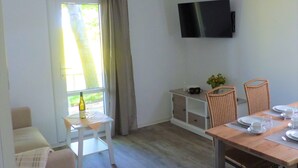 A room with a dining table set for two, a TV mounted on the wall, and a window with curtains. - Bernsteinland Barth (Barth)