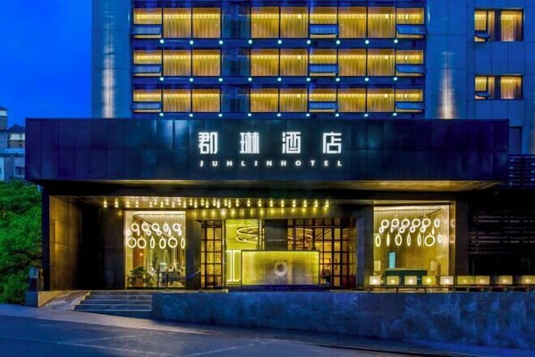 Un hôtel Junlin à la façade moderne, aux fenêtres illuminées et à l’entrée bien visible, avec des marches menant à la porte.