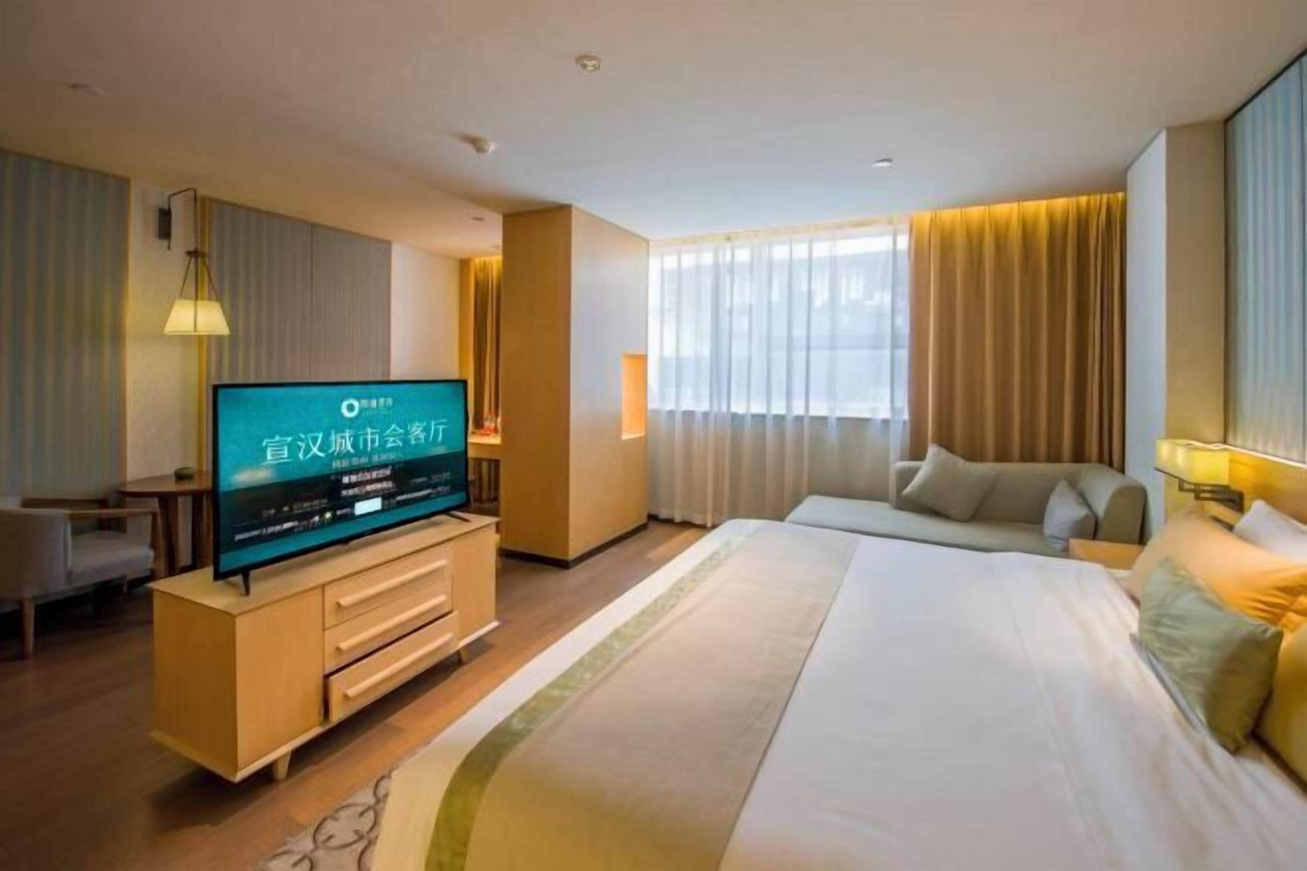 A hotel room with a bed, a TV, a desk, and a sofa.
