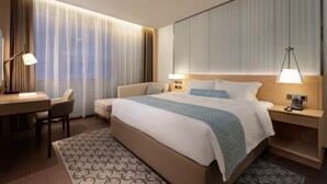 Moderni hotellihuone, jossa on suuri sänky, yöpöydät lampuineen, työpöytä ja tuoli.