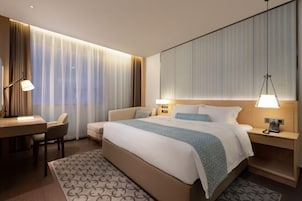 Una habitación de hotel moderna con una cama grande, mesitas de noche con lámparas, un escritorio y una silla.