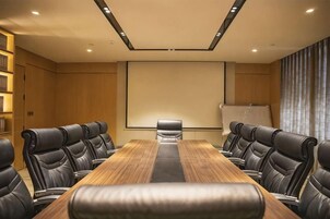 Una sala de conferencias con una larga mesa y sillas de cuero, una pizarra y una pantalla de proyector.