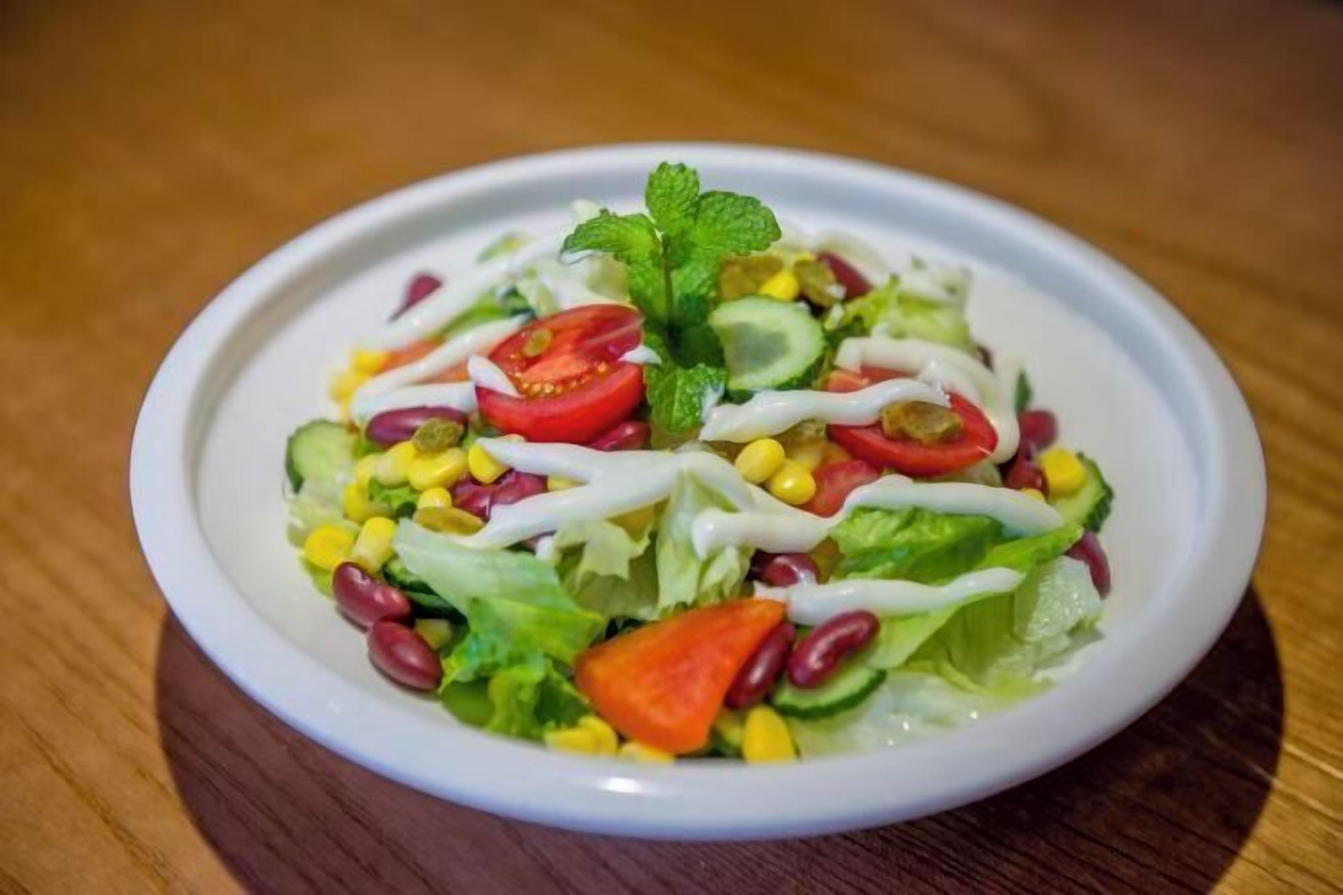 Un saladier rempli de salade, avec divers légumes et garni de feuilles de menthe.
