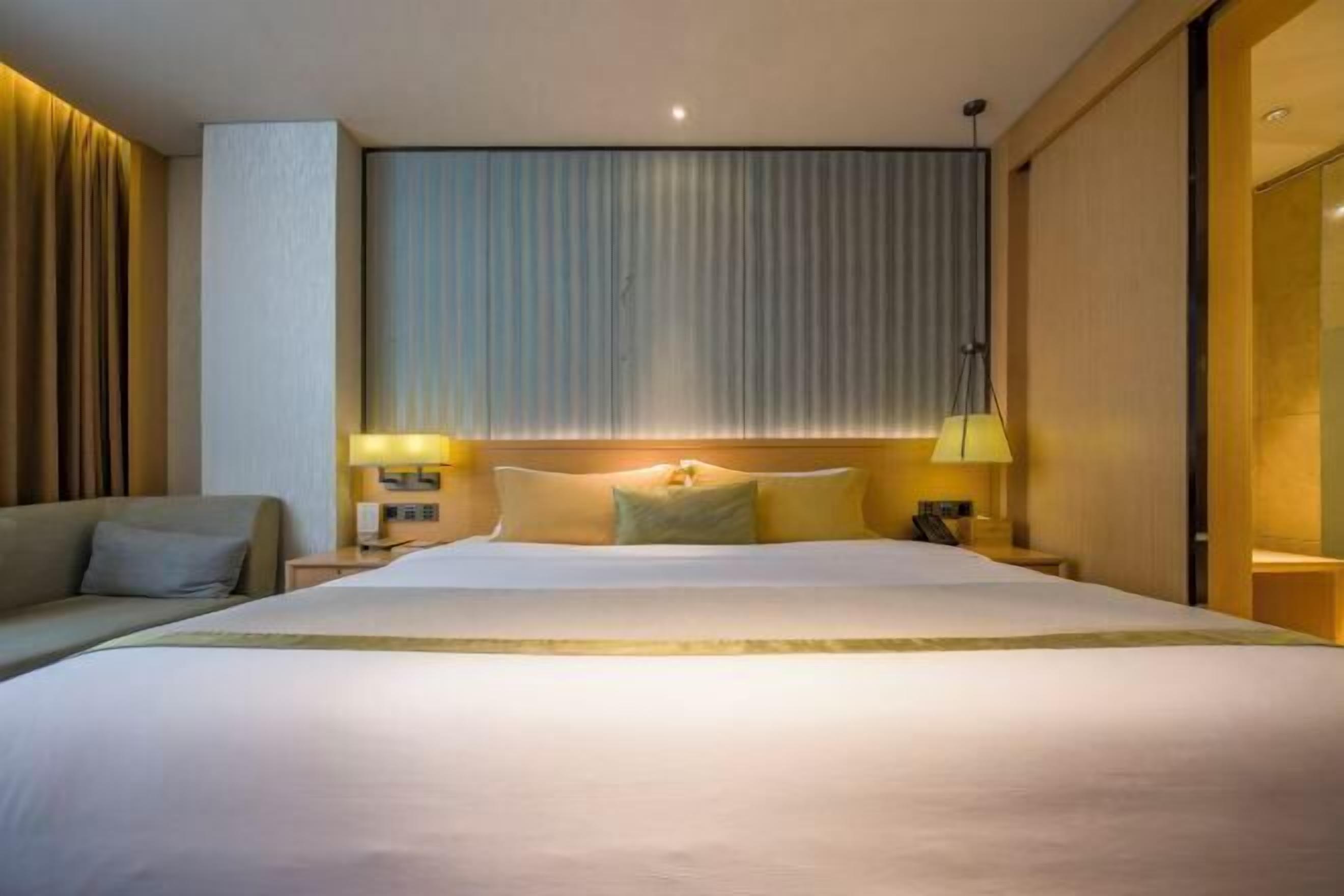 A hotel room with a large bed, two bedside tables with lamps, a sofa, and a large window with curtains.