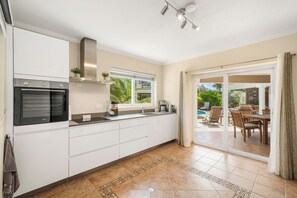 Une cuisine moderne dotée d’un four encastré, d’une fenêtre et d’une porte-fenêtre coulissante donnant sur un espace repas extérieur.