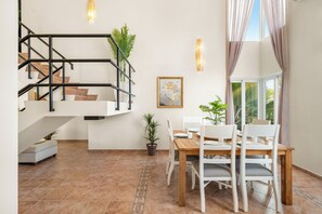 Un intérieur moderne comprenant un escalier, une table à manger, des chaises, des plantes en pot et une œuvre d’art encadrée.
