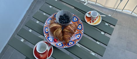 A balcony with a table set for breakfast, including croissants, a bowl of blueberries, and a cup of coffee.