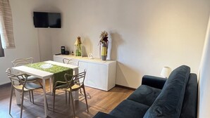 A modern living space with a dining area, a black sofa, and a flat-screen TV mounted on the wall.