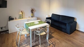 A dining area with a table and chairs, a black sofa, and a white console table with a lamp and decorative items.