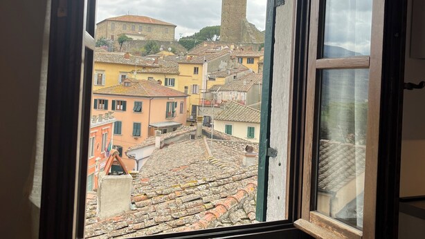 A window with a view of a historic town, including a prominent tower and colorful buildings.