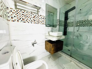 A modern bathroom with a glass shower enclosure, a white sink with a marble countertop, and a wooden vanity. - Presken Waters (Lagos)