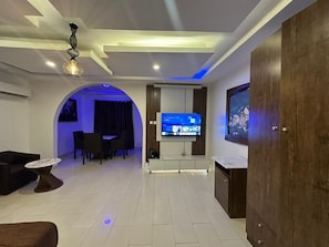A modern living room with a flat-screen TV, a dining area, and a wooden cabinet. - Presken Waters (Lagos)