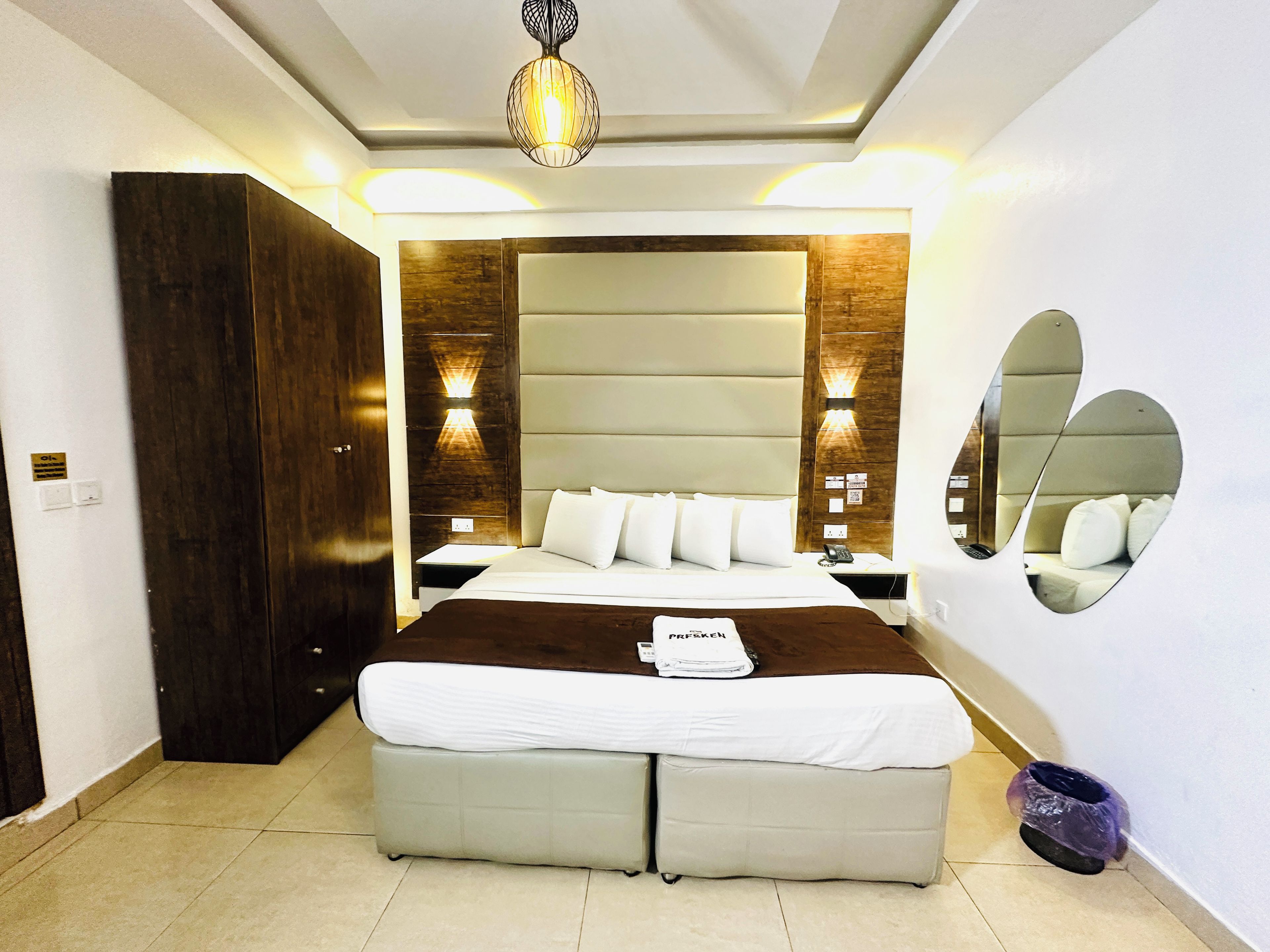 A modern hotel room with a large bed, a wardrobe, a bedside table, and a mirror on the wall.