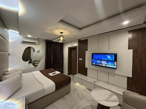 A modern hotel room with a bed, a TV mounted on the wall, a small round table, and a ceiling light. - Presken Waters (Lagos)