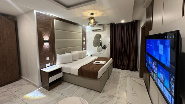 A modern bedroom with a large bed, a TV, a bedside table, and a built-in headboard. - Presken Waters (Lagos)