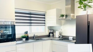 Eine moderne Küche mit weißen Schränken, einem Einbauofen, einer Kaffeemaschine und einem schwarzen Kühlschrank.