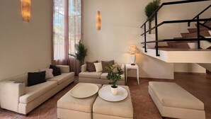 Ein modernes Wohnzimmer mit einer Sofagarnitur, Hocker, einer Lampe und einer Treppe.