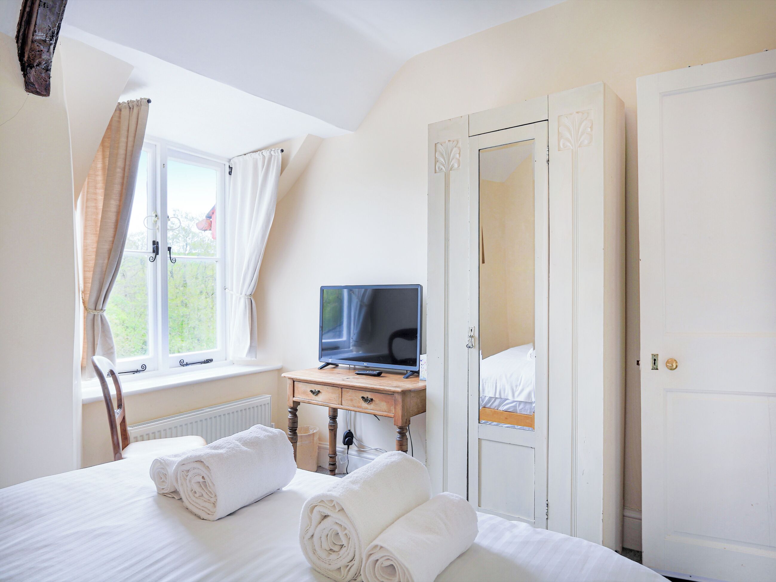 A hotel room with a bed, a desk with a television, a wardrobe, and a window with curtains.