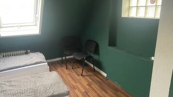 Ein Zimmer mit zwei Betten, einem Sessel, einem Heizkörper und einem Fenster mit Jalousien.