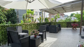 Un espace extérieur aménagé en terrasse, avec des meubles en osier, une table agrémentée d’un arrangement floral et un coin salon abrité.