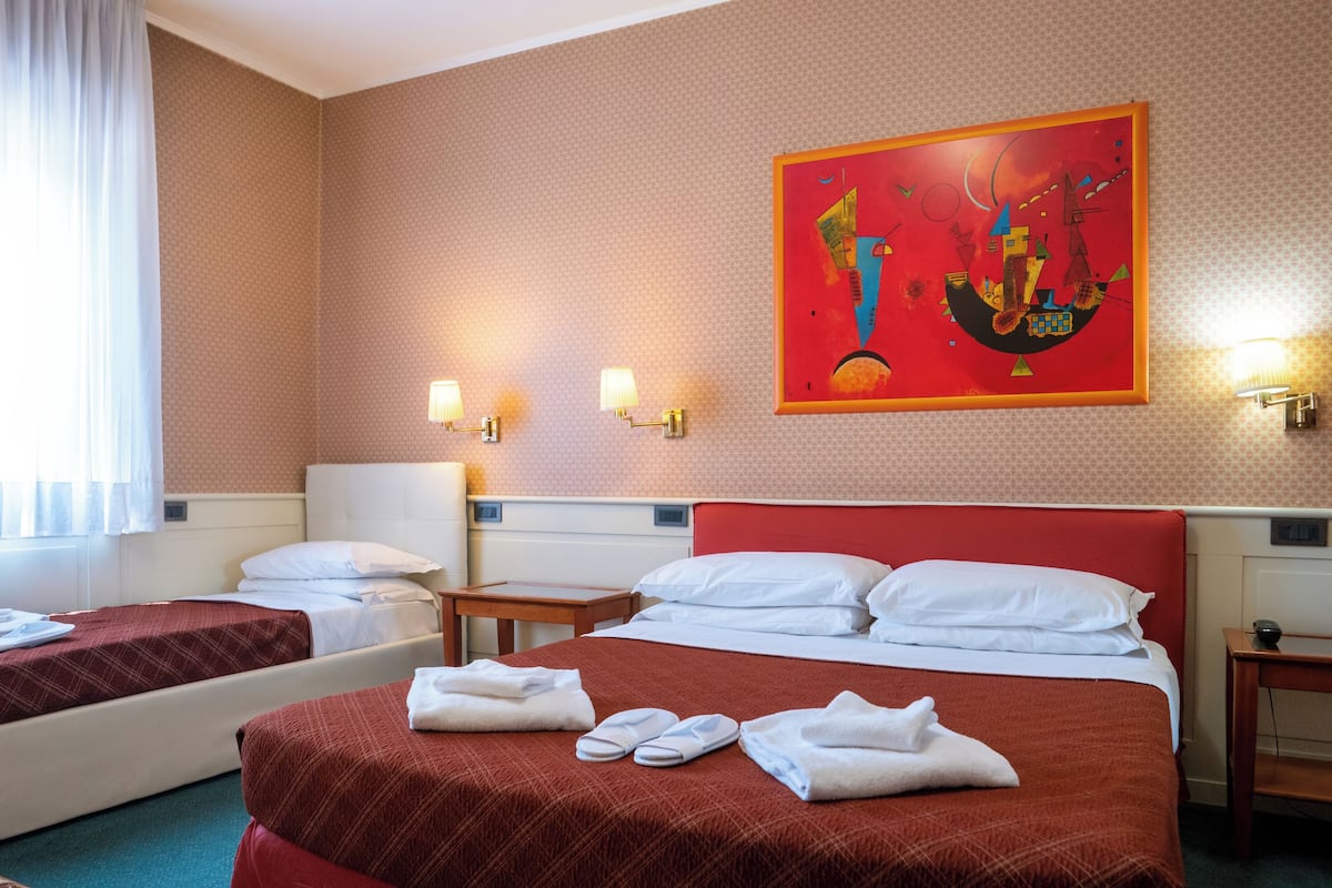 A hotel room with two beds, a red headboard, a painting on the wall, and two bedside lamps.
