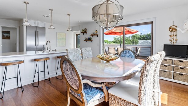 Cozinha moderna com eletrodomésticos de aço inoxidável, área de jantar com mesa redonda e banquetas de bar, e uma grande janela com vista para o verde.