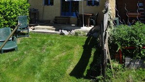 Une maison rustique en bois, avec un toit en tuiles, une terrasse dotée d’une table et de chaises, et un grand parasol.