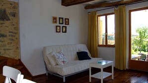 Une pièce avec un canapé blanc, une petite table blanche et une fenêtre avec des rideaux. Quatre tableaux encadrés sont accrochés au mur.