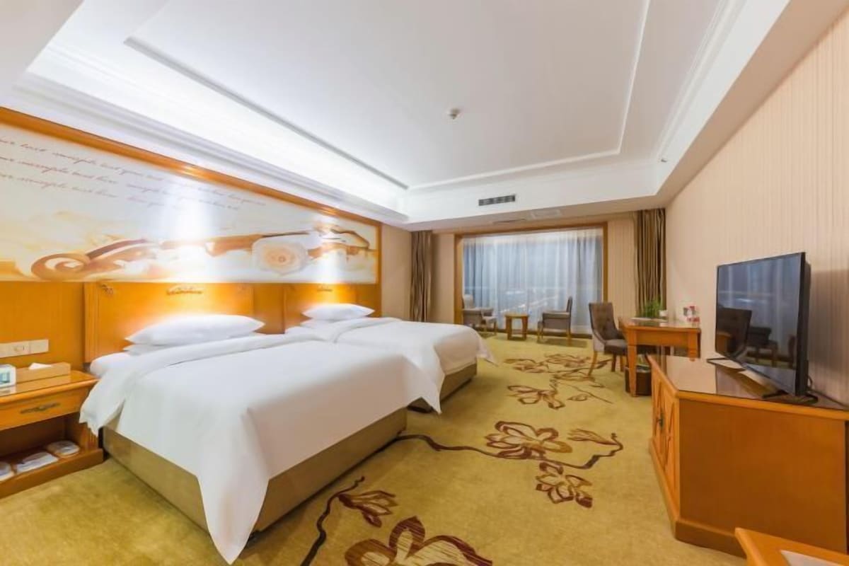 Une chambre d’hôtel avec un grand lit, un bureau, une télévision et une fenêtre avec des rideaux.