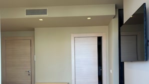 Un dormitorio con cama, armario, televisor integrado y rejilla de ventilación en el techo.