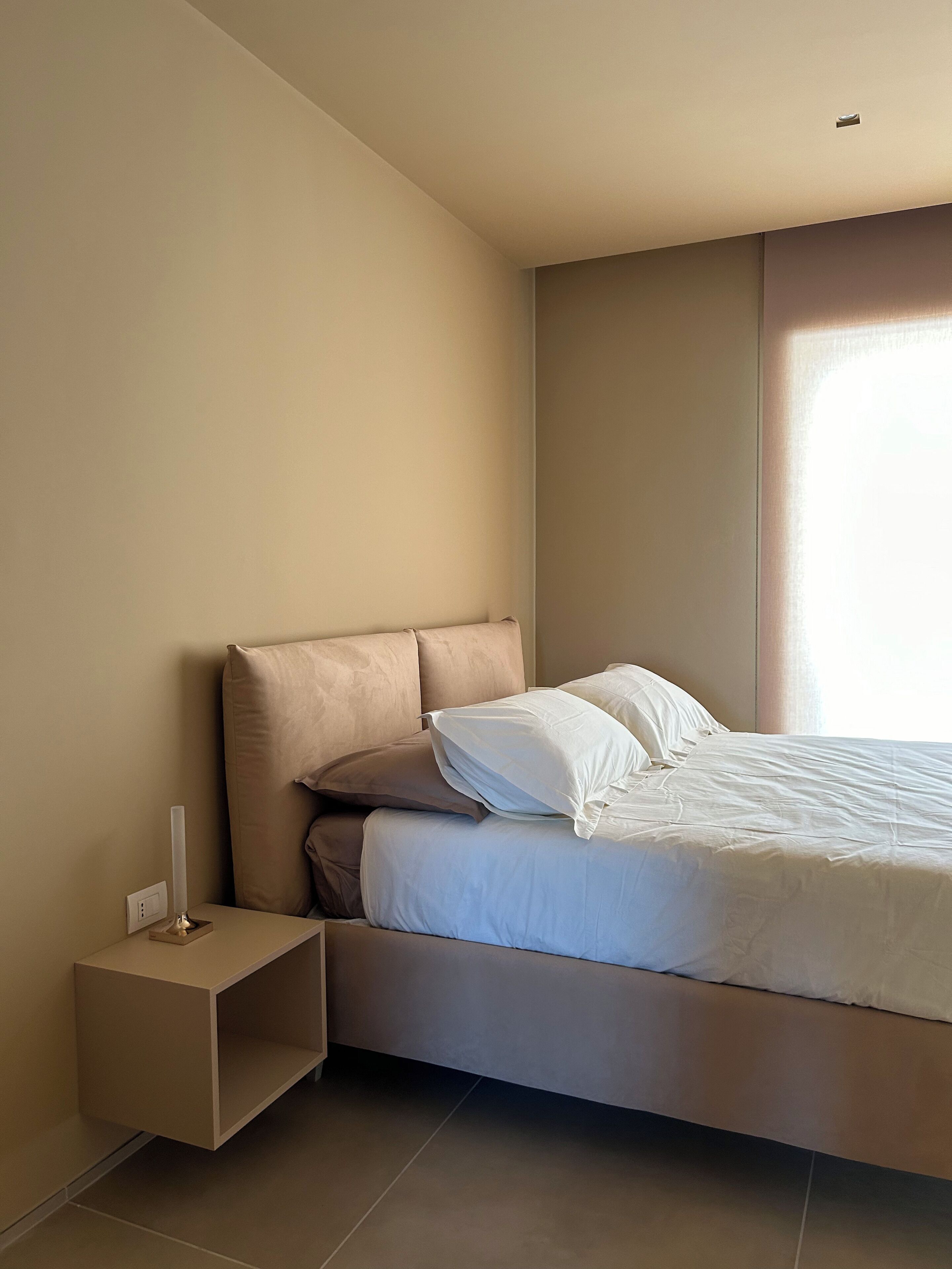A modern bedroom with a bed, a nightstand, and a window.