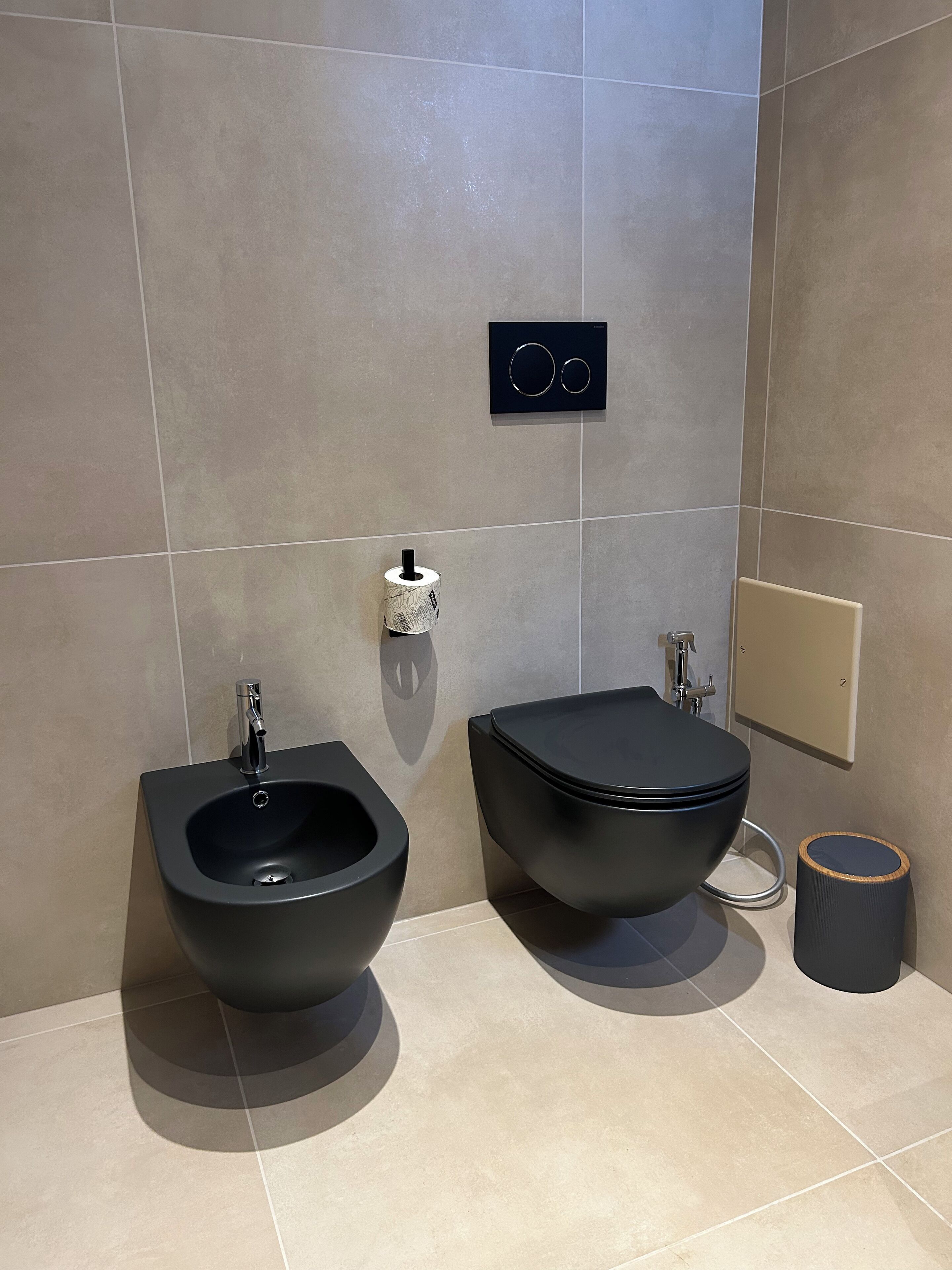 A modern bathroom with a bidet, a toilet, and a trash can.
