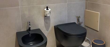A modern bathroom with a bidet, a toilet, and a trash can.