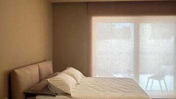 A modern bedroom with a large bed, a nightstand, and a window with a view.