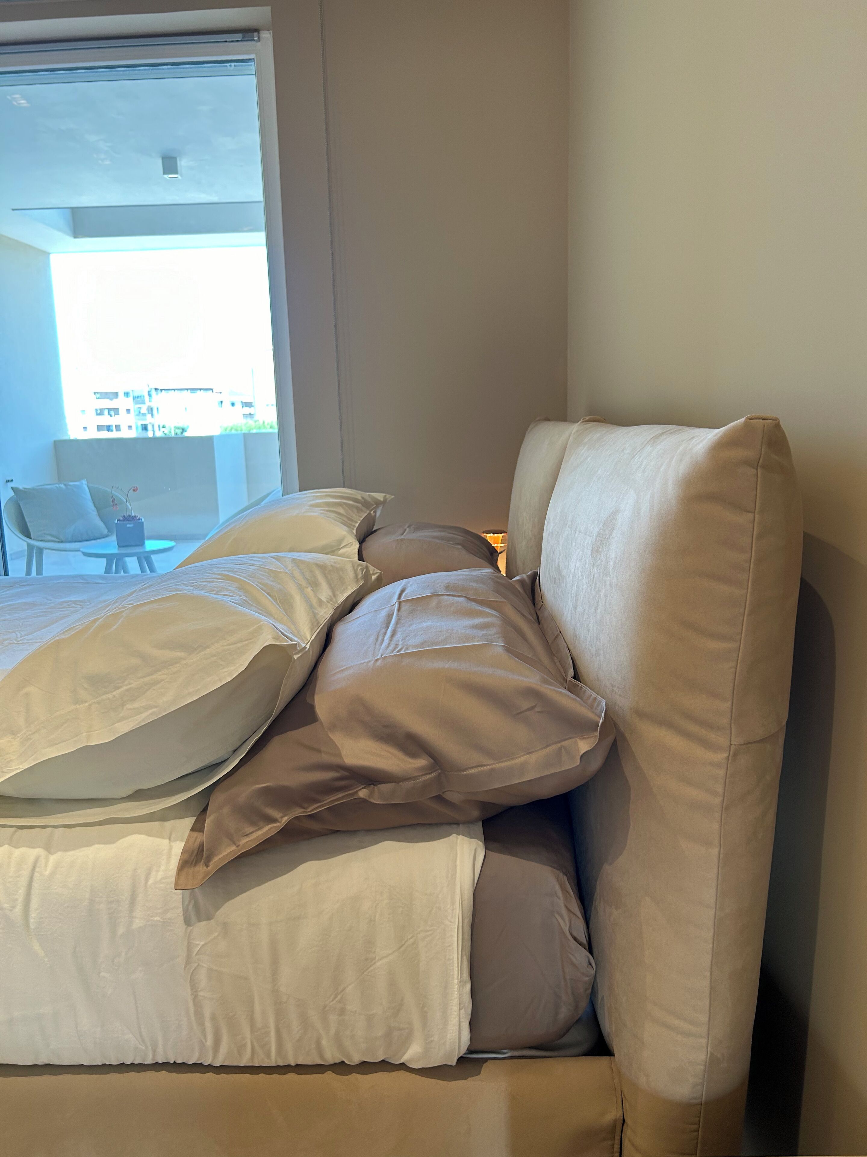 Un letto con biancheria da letto bianco e beige, una sedia e un comodino con una lampada.