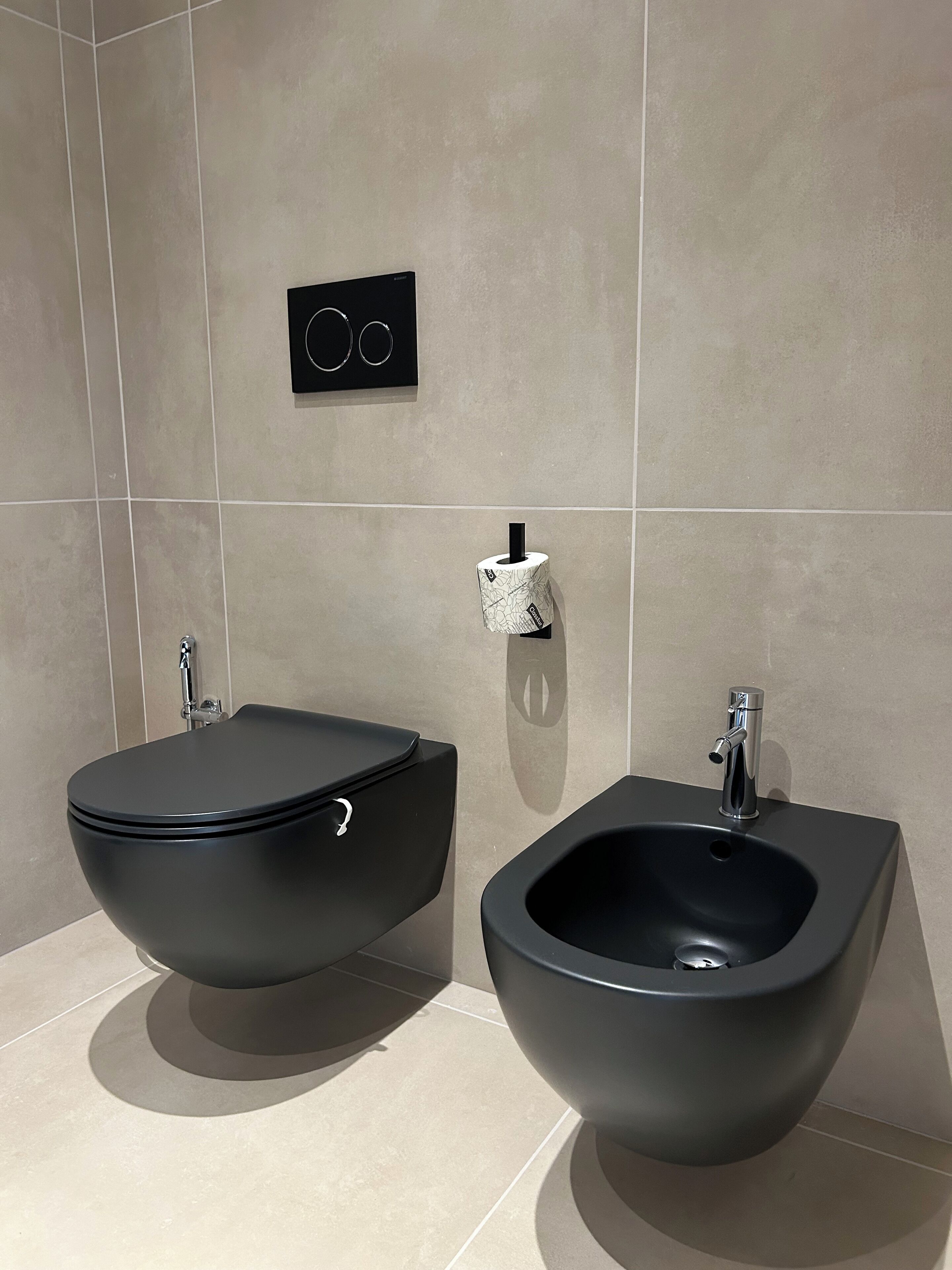 A modern bathroom with a bidet, a toilet, and a wall-mounted bidet paper holder.