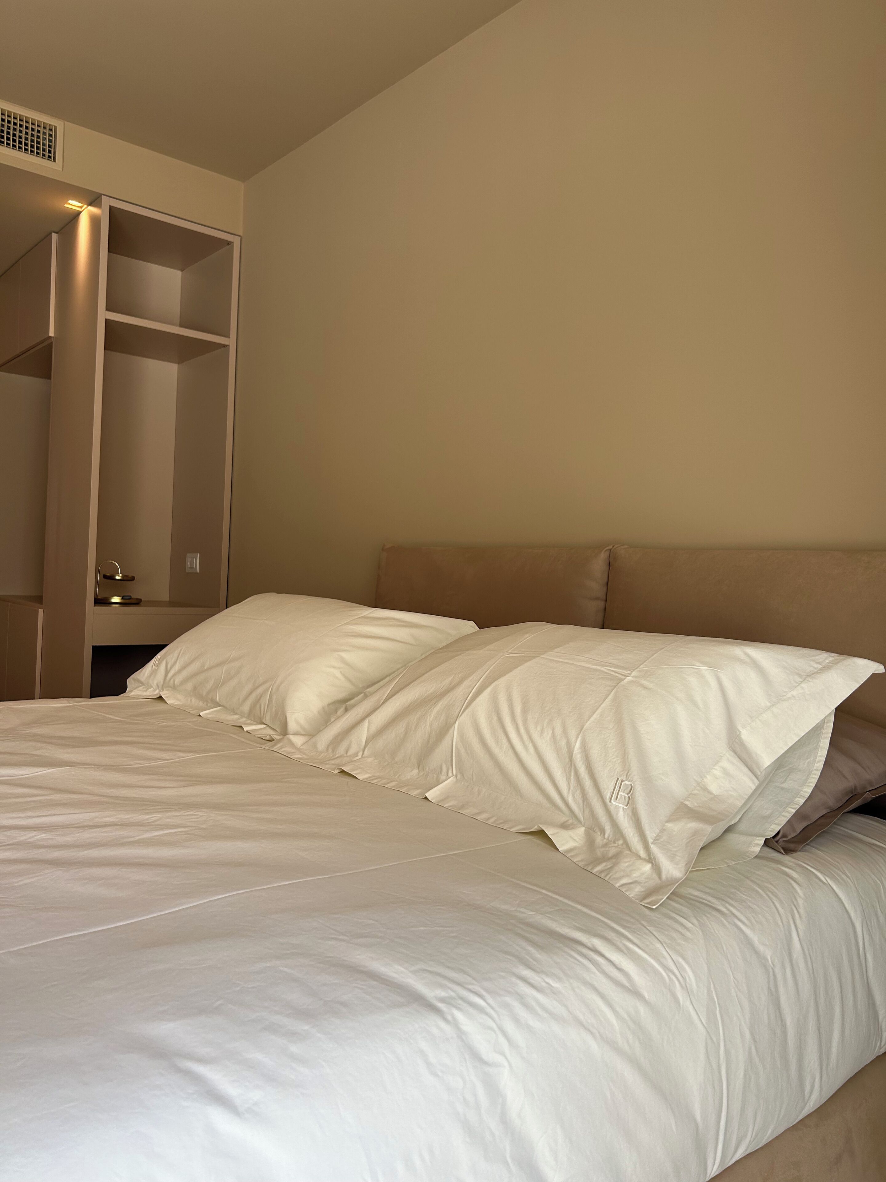 A neatly made bed with white linens in a room with a sloped ceiling and built-in shelving.