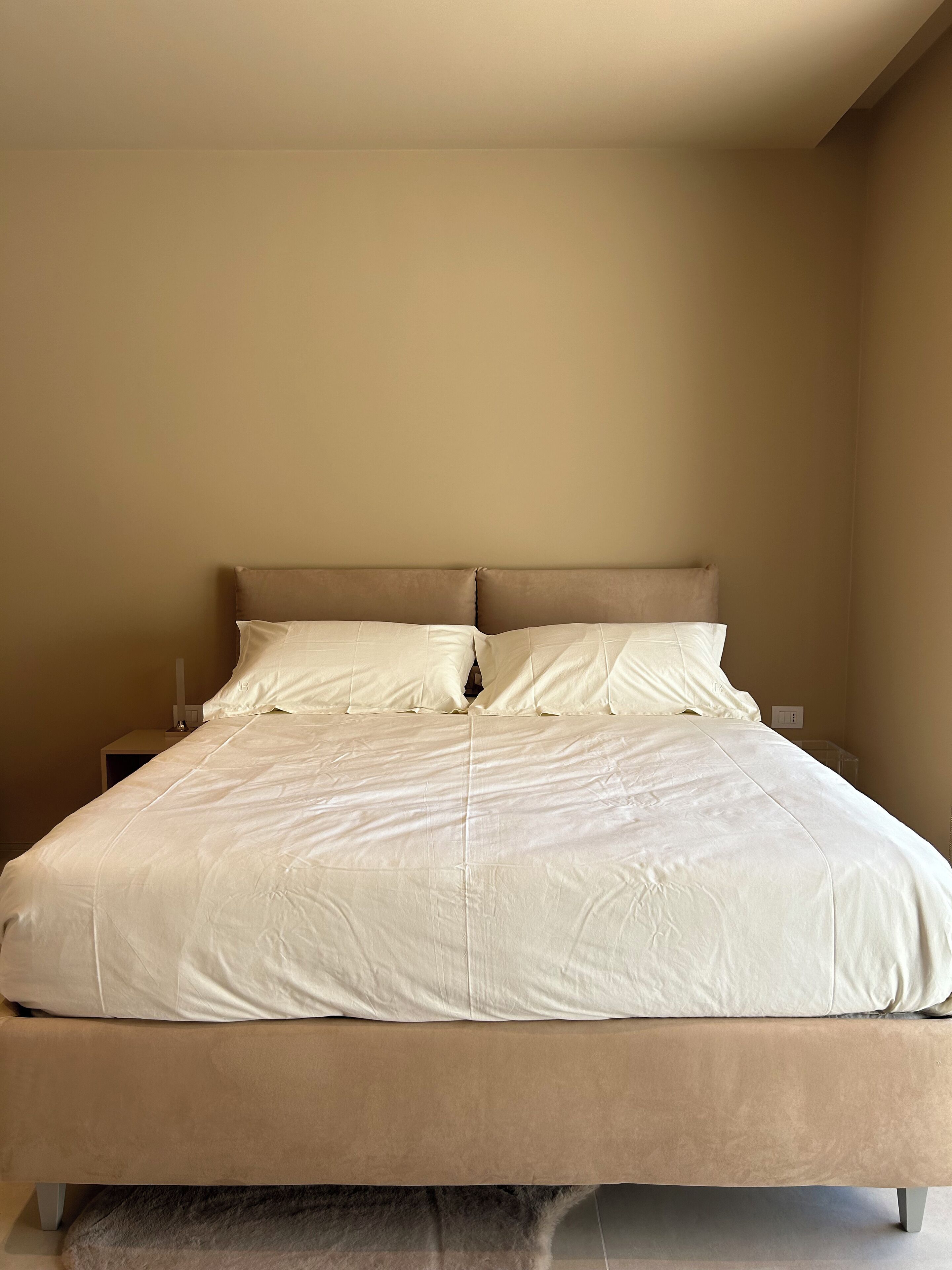 Una cama con cabecera, una mesita de noche y un enchufe de pared.