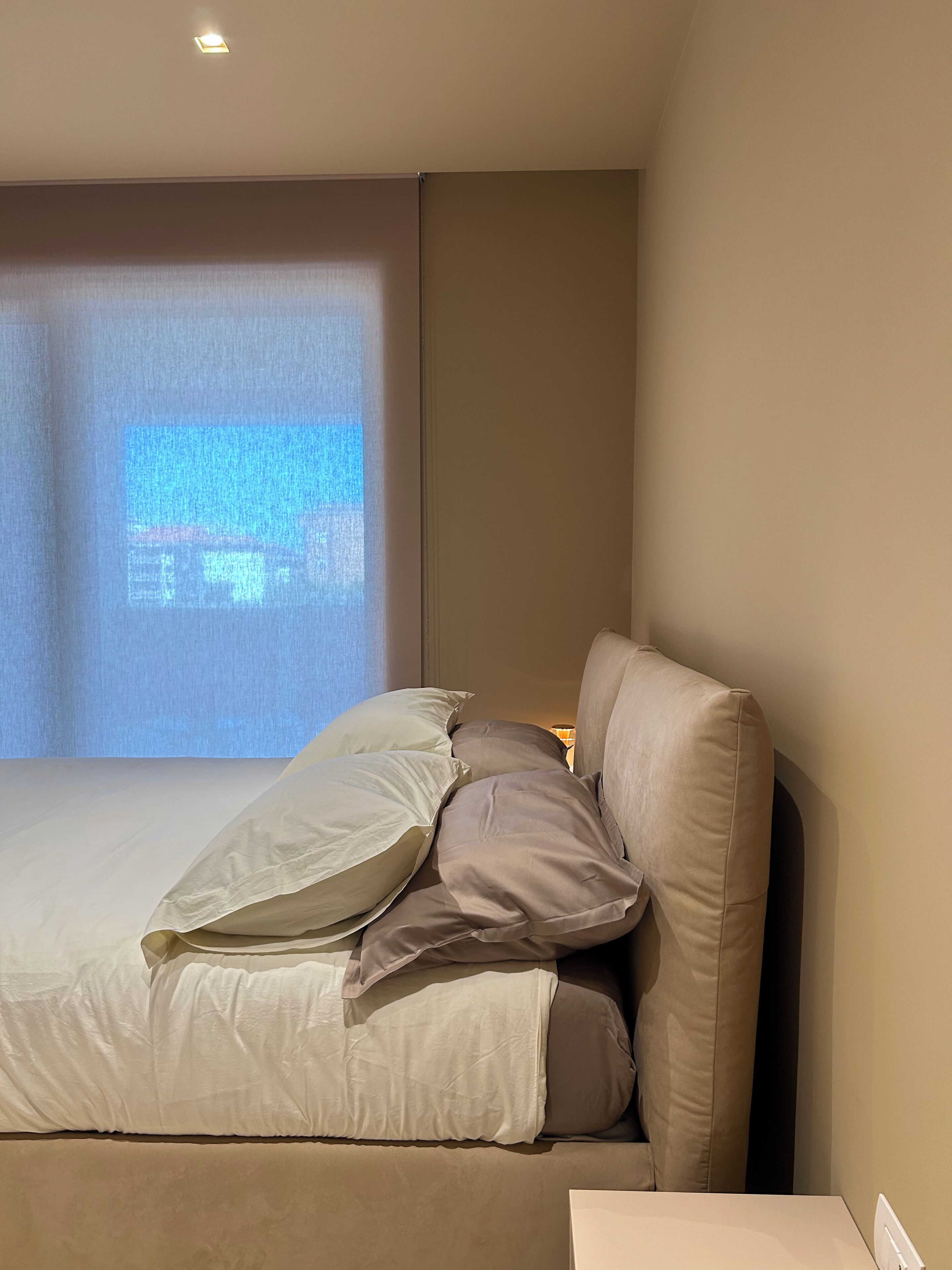 A bedroom with a bed, pillows, a nightstand, and a wall-mounted projector.