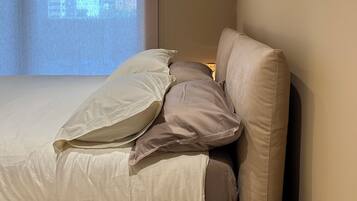 Un dormitorio con cama, almohadas, una mesita de noche y un proyector de pared.