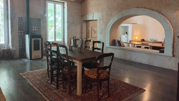 Un comedor con una gran mesa de madera, varias sillas, un tapete estampado y una chimenea de piedra.