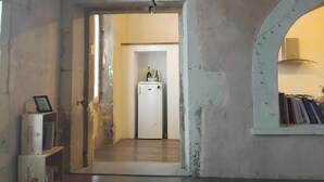 Un espacio habitable integrado con piso de madera, un refrigerador blanco y un acceso a otra habitación.