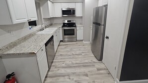 A narrow kitchen with white cabinets, a stainless steel refrigerator, a microwave, and an oven. - Renovated contemporary home centrally located (Gainesville)