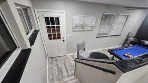 A modern interior with a pool table, a door with a glass panel, and a staircase with wooden flooring. - Renovated contemporary home centrally located (Gainesville)
