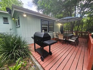 A covered outdoor deck with a grill, dining table, and chairs. - Renovated contemporary home centrally located (Gainesville)