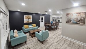 A modern living room with a dark accent wall, a dining area with a wooden table and chairs, and a large painting on the wall. - Renovated contemporary home centrally located (Gainesville)