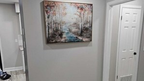 A hallway with a wooden floor, a white door, and a painting of a forest scene. - Renovated contemporary home centrally located (Gainesville)