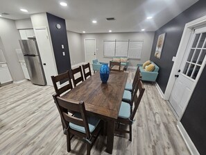 A modern kitchen with a wooden dining table, chairs, a refrigerator, and a blue vase. - Renovated contemporary home centrally located (Gainesville)