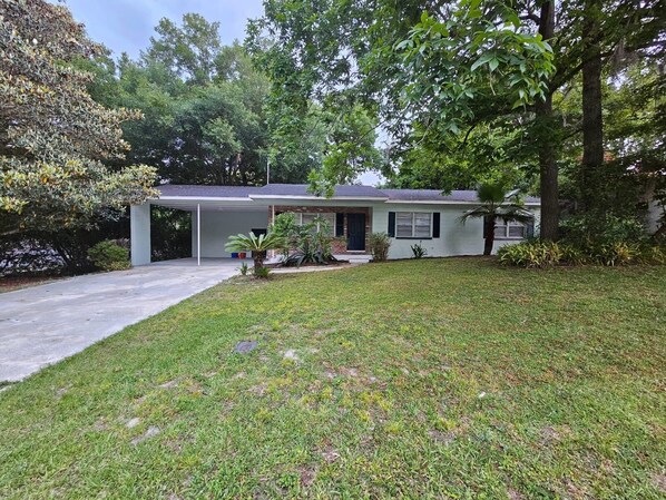A single-story house with a covered garage, a front lawn, and a variety of trees and shrubs. - Renovated contemporary home centrally located (Gainesville)