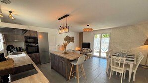 Una cocina moderna con una isla central, un comedor con sillas blancas y un televisor en la sala de estar.